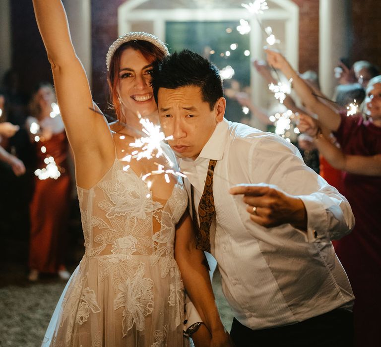 Bride & groom hold sparklers surrounded by friends & family 