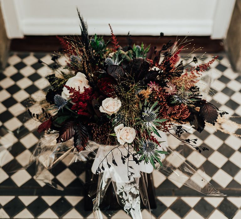 Wedding bouquet with roses, thistle, autumn leaves and more foliage for autumnal gothic wedding with a black wedding cake 