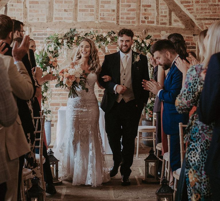 Bride in lace mermaid wedding dress walking back down the aisle with the groom as a married couple at the rustic Stanlake Park wedding