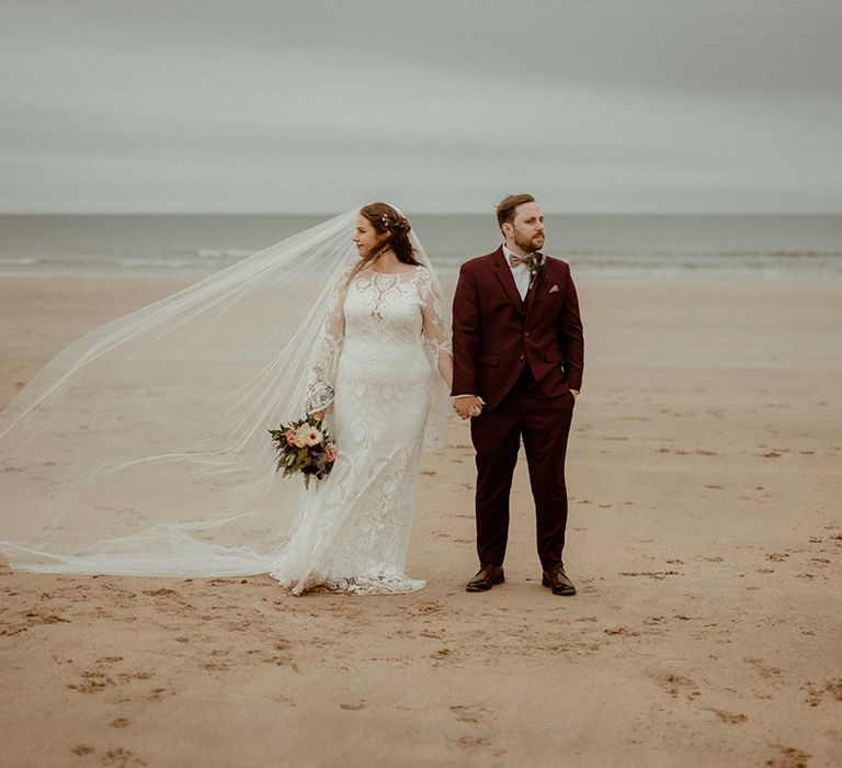 Bell sleeve wedding dress from Rue De Seine worn by the bride with the groom in a burgundy suit for their coastal wedding 