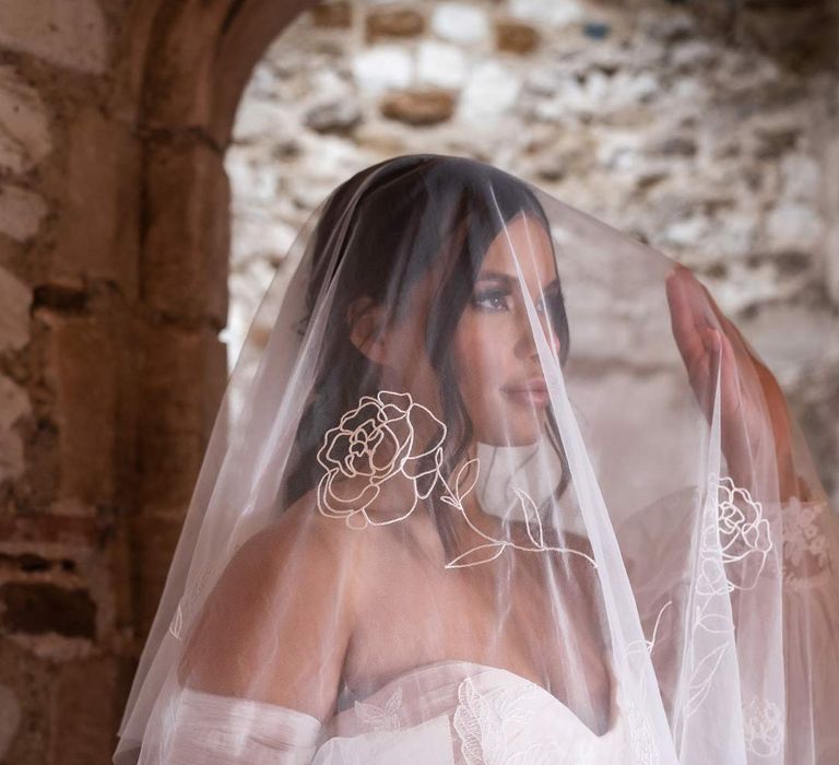 Bride in off the shoulder wedding dress with detachable puff tulle sleeves holding personalised embroidered wedding veil at Pentney Abbey wedding