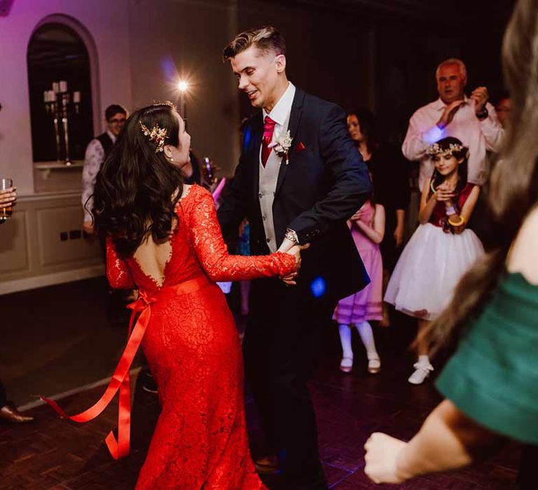 Bride in v-back bow detail reception dress - red lace wedding dress with long sleeves, red and gold hair accessories and golden closed toe wedding heels