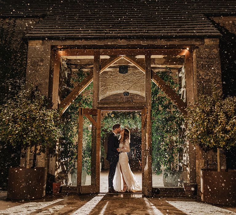 The bride and groom share a special moment together on the snowy evening of their winter wedding at the entrance to Stone Barn