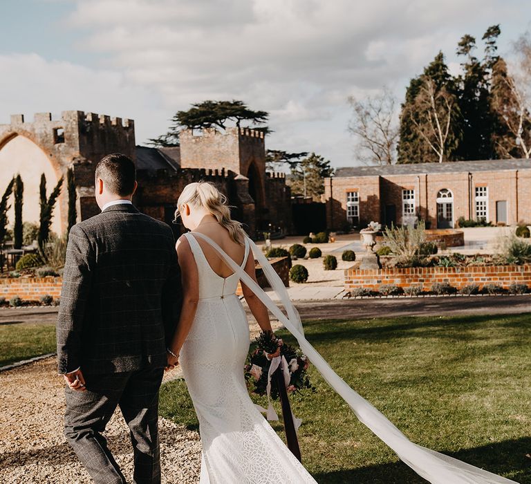 Bride in fitted wedding dress by Karen Willis Holmes with tulle wings walking with the groom at country house wedding 