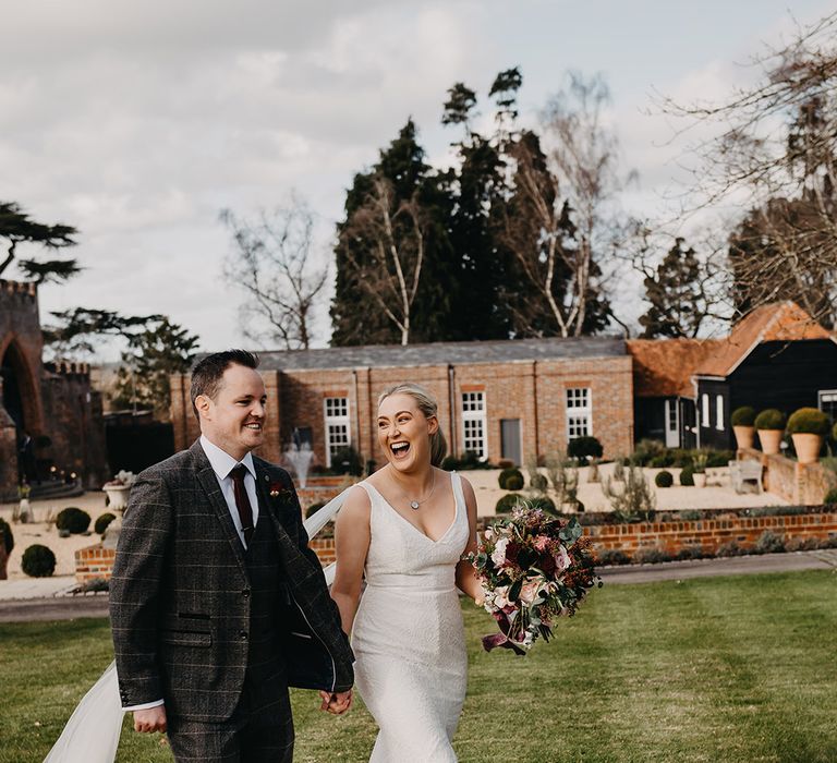 Bride in fitted wedding dress walking hand in hand with the groom on their wedding day at Wasing Park 