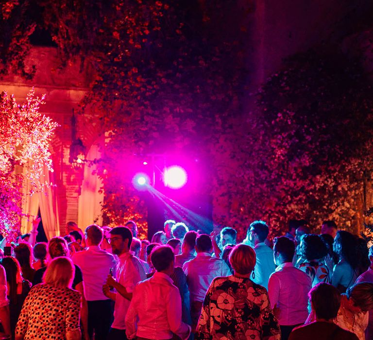 The wedding guests party at the wedding reception with colourful lights 