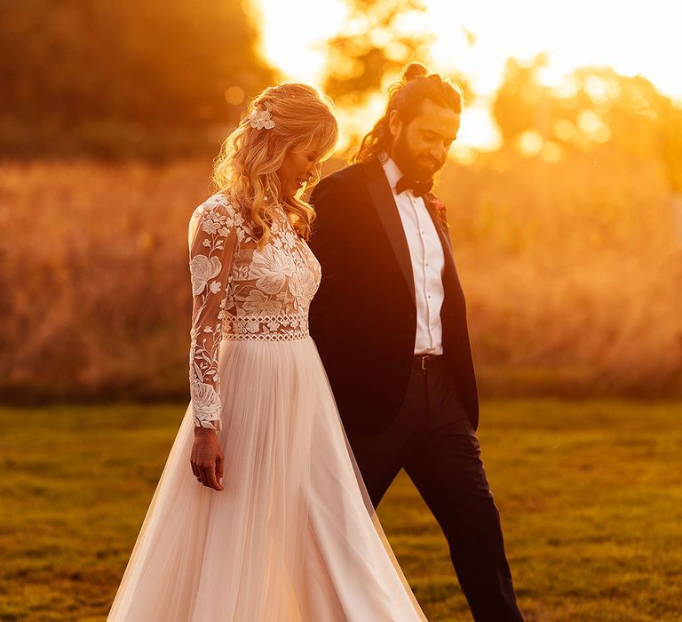 Groom in black tie with bride in lace long sleeve wedding dress at sunset 