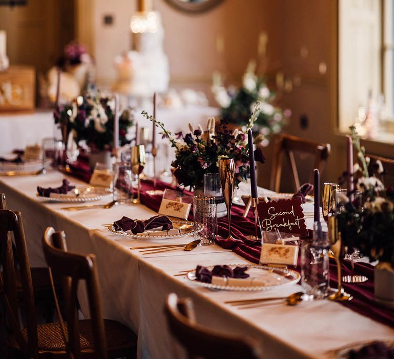 Burgundy wedding tablescape for winter wedding with beaded charger plates, gold rimmed glasses and table name signs 