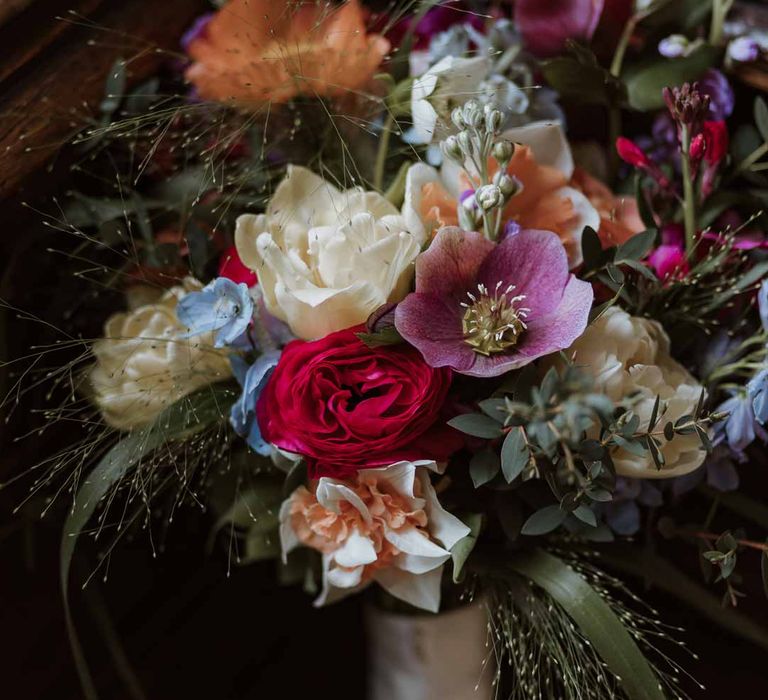 Colourful spring bridal bouquet with roses, peonies, carnations and foliage wrapped with ivory silk ribbon