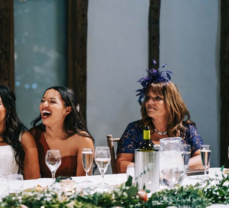 Wedding guests and bride laughing during wedding speeches by a rustic wedding tablescape at South Farm wedding