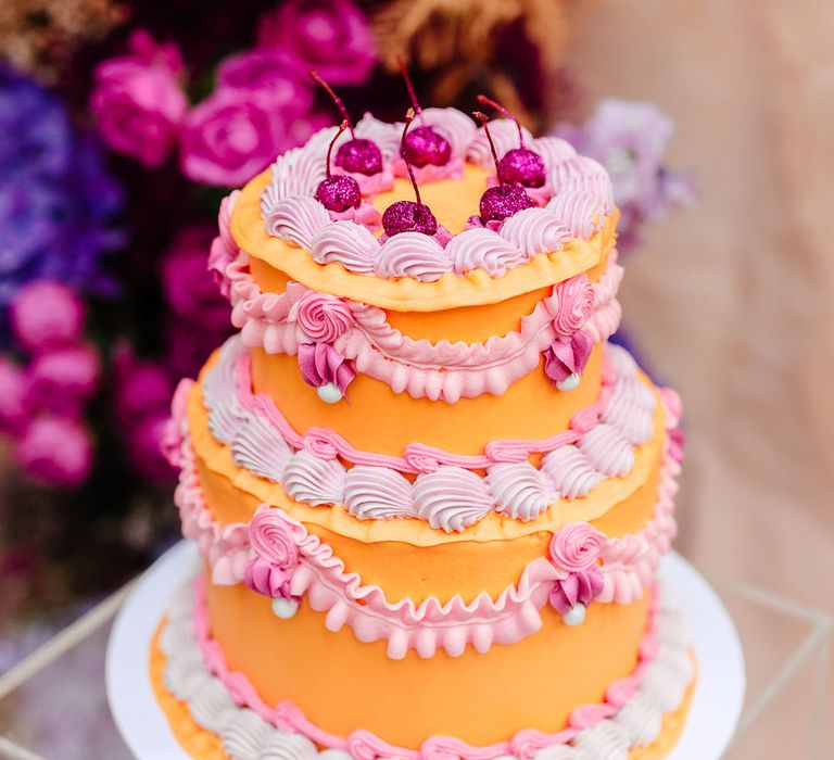 Peach and lilac wedding cake with kitsch style piping work decorated with glitter dipped cherries 