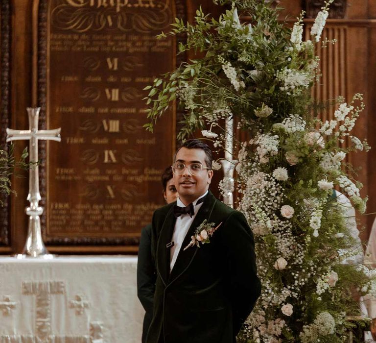 bottle green velvet grooms suit, black bowtie and chic boutonniere standing at the alter of Inner Temple Hall