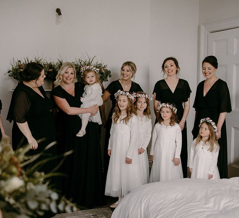 Bridesmaids in black high street bridesmaid dresses with flower girls in white dresses and flower crown 