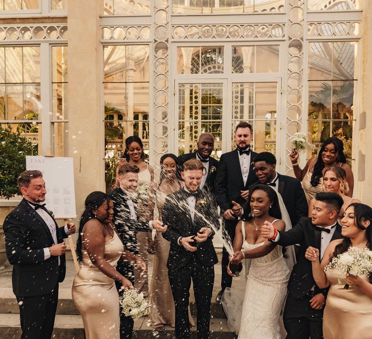 Epic champagne spray wedding photo of the bride and groom with their wedding party 