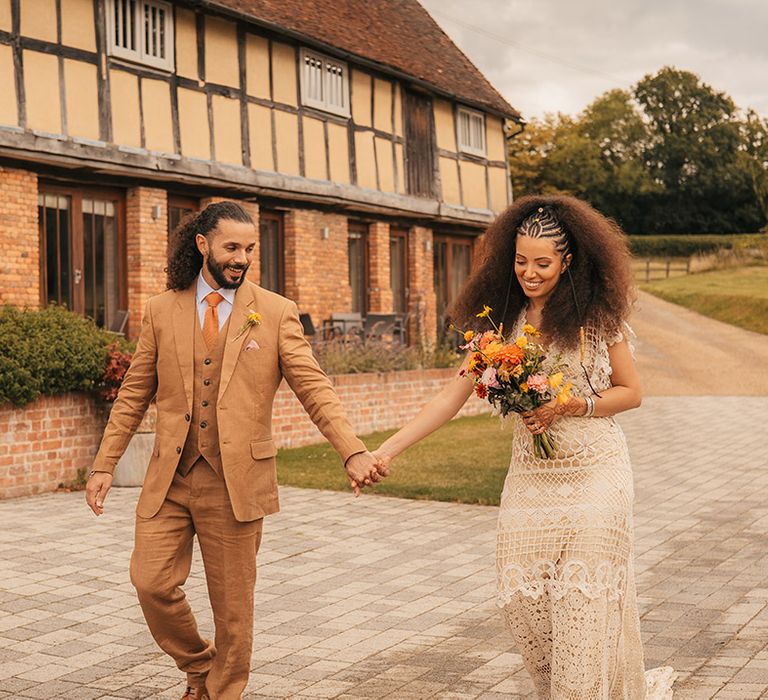 The Oak Barn wedding venue with the bride and groom walking outside the grounds wearing retro wedding outfits 