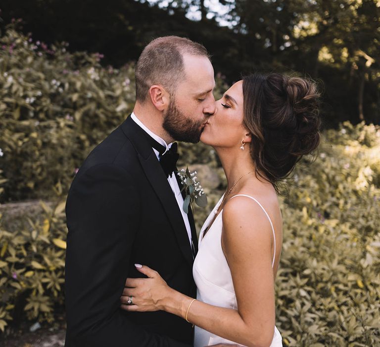 Bride in satin bridal gown kisses the groom in a black tuxedo at Bowers Mill 