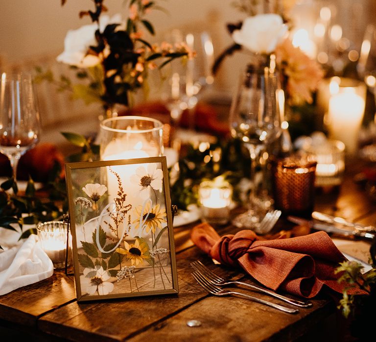 Autumnal wedding flower arrangements decorating the tablescape with pressed wildflowers in a gold photo frame for table number sign