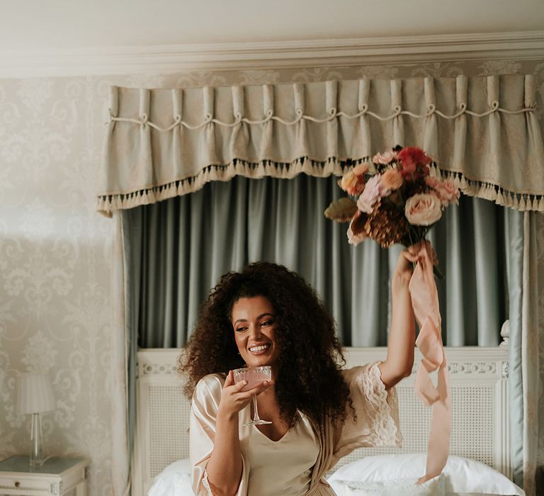 Bride holding up autumnal wedding bouquet in gold satin pyjamas and robe 