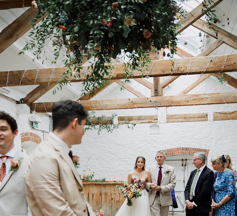 Bride in floral strapless Nicole Milano wedding dress walking down the aisle with the father of the bride 