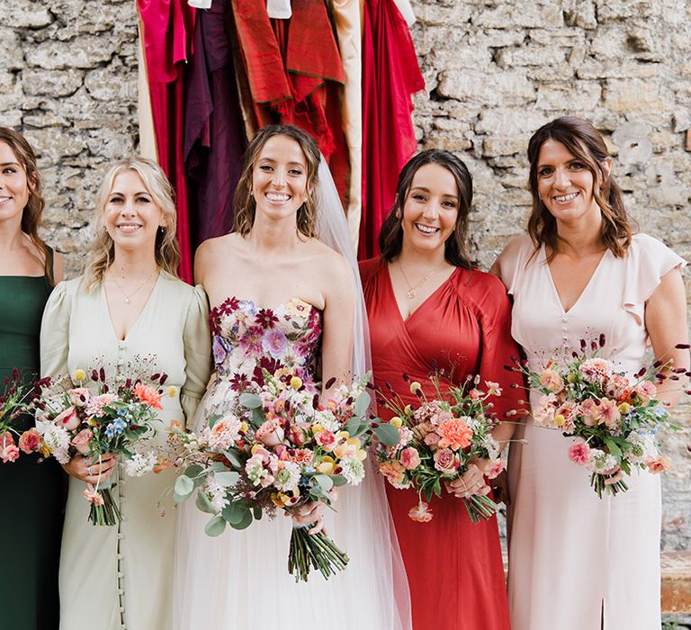 Bride with bridal party in mismatched bridesmaid dresses with colourful bouquets for summer wedding 