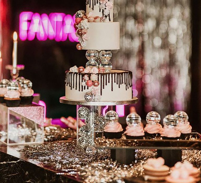 Wedding cake adorned with disco balls on dessert table at wedding by Susana Ríos Photography