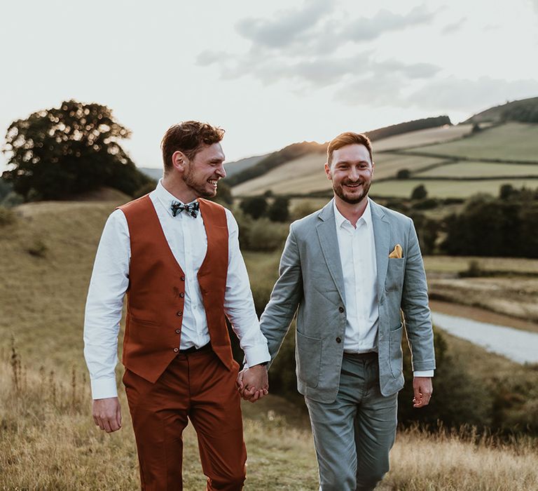 Groom in orange waistcoat with groom in grey wedding suit walking around the stunning scenery at their venue 