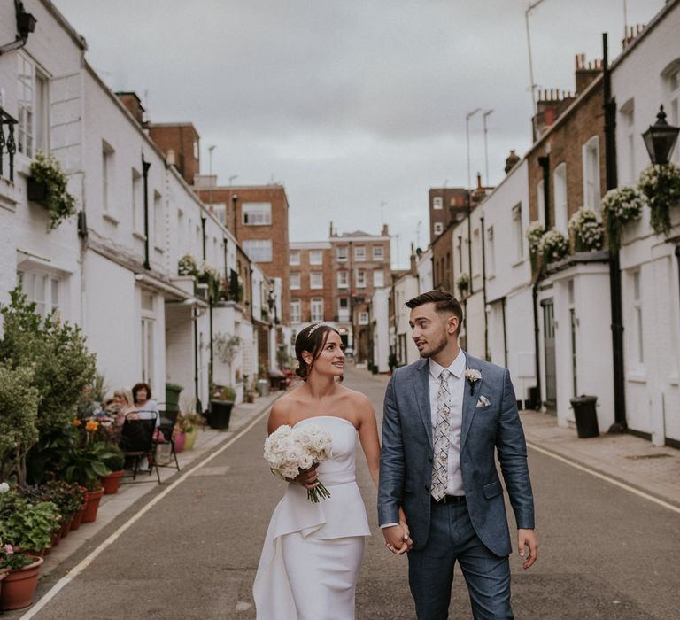 Bride in layered Roland Mouret dress with white bouquet holding hands with her husband