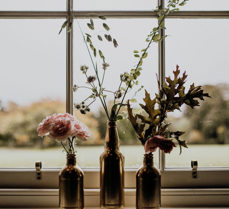 Three beer bottle vases with roses and foliage for boho wedding decor