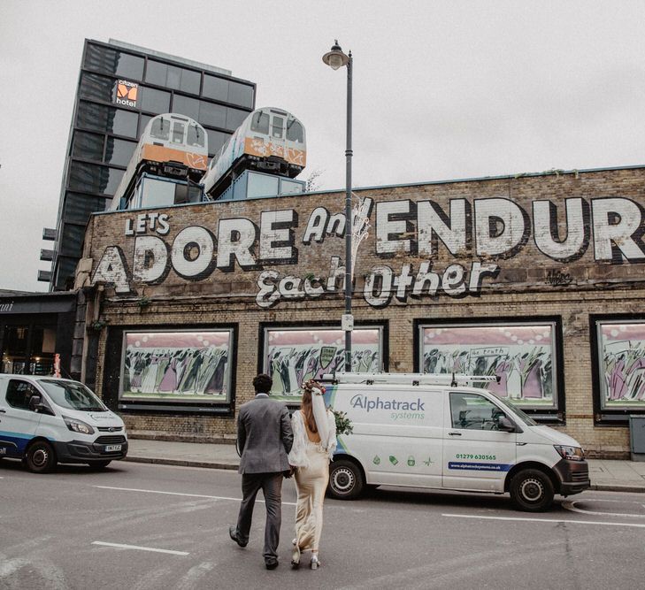 Wedding couple cross the road in front of a building that reads "Let's adore and endure each other"