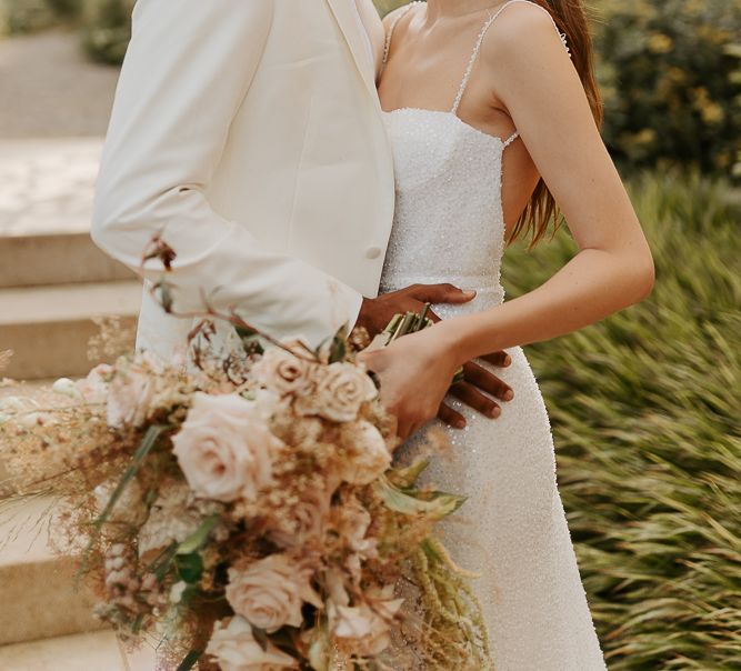 Black groom with afro hair and white tuxedo jacket kissing his brides head with long brown hair and red lipstick in a sparkly wedding dress with thin straps 