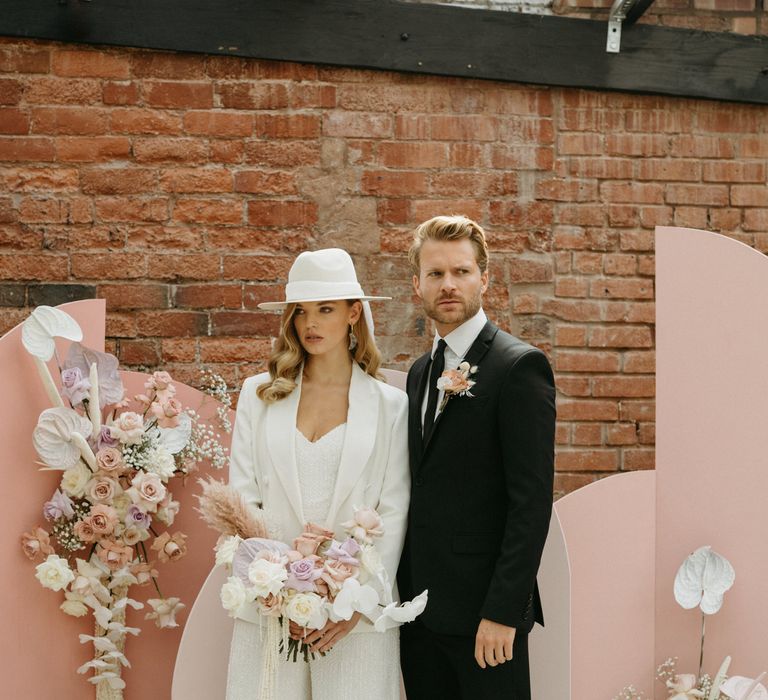 Bride and groom standing at the altar with pink board backdrop and pastel pink and purple flowers 