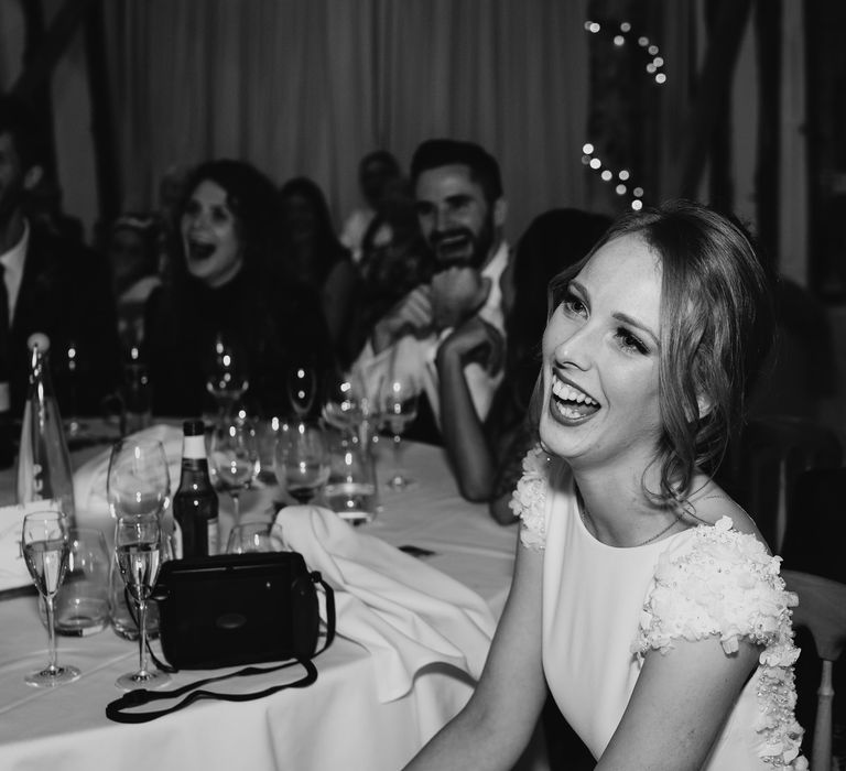 Bride in a fitted wedding dress with appliqué cap sleeve detail smiling during the evening reception 