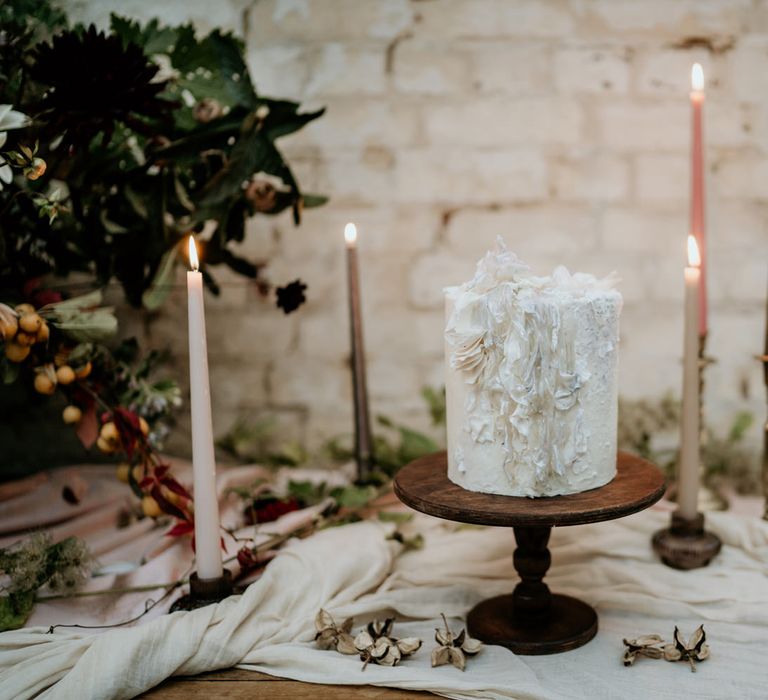 Single tier wedding cake for elopement wedding resting on a wooden cake stand surrounded by coloured taper candles 