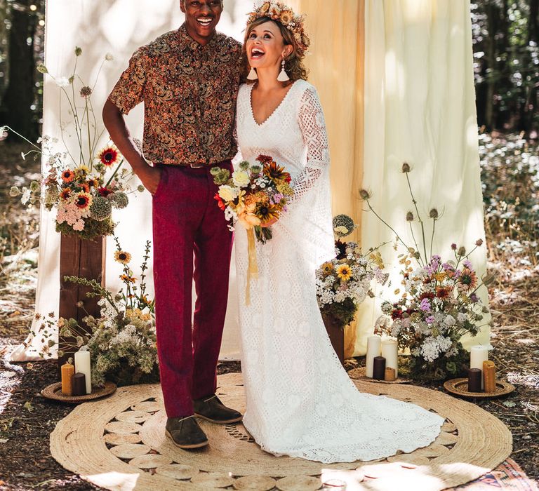 A bride and groom stand in front of a ceremony set up in the woods. 