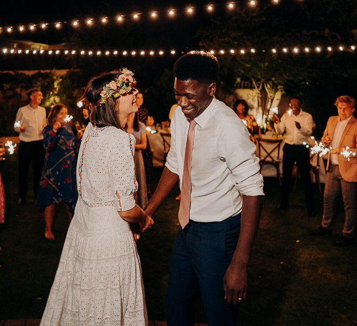 outdoor wedding first dance under a canopy of festoon lights and surrounded by guests waving sparklers