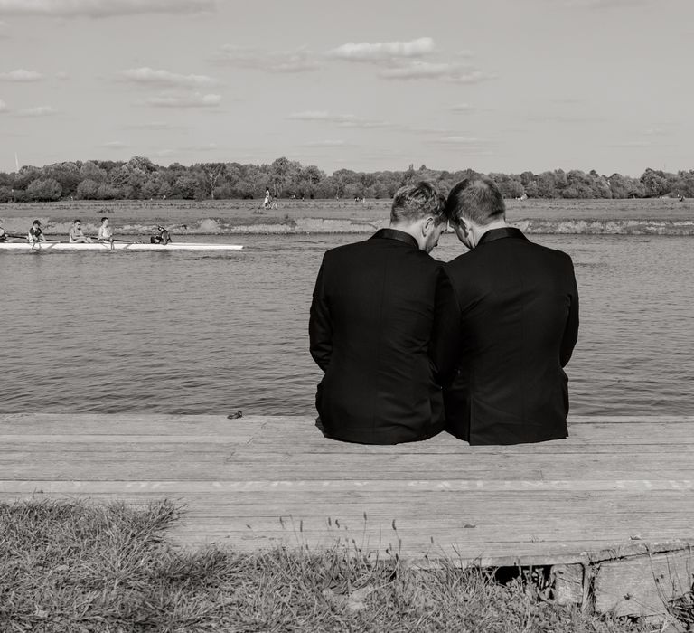 Grooms sit together in black & white image in front of river