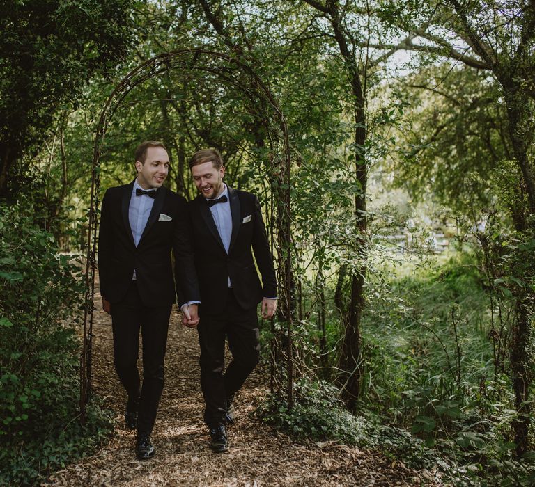 Grooms walk through green floral archway on wedding day