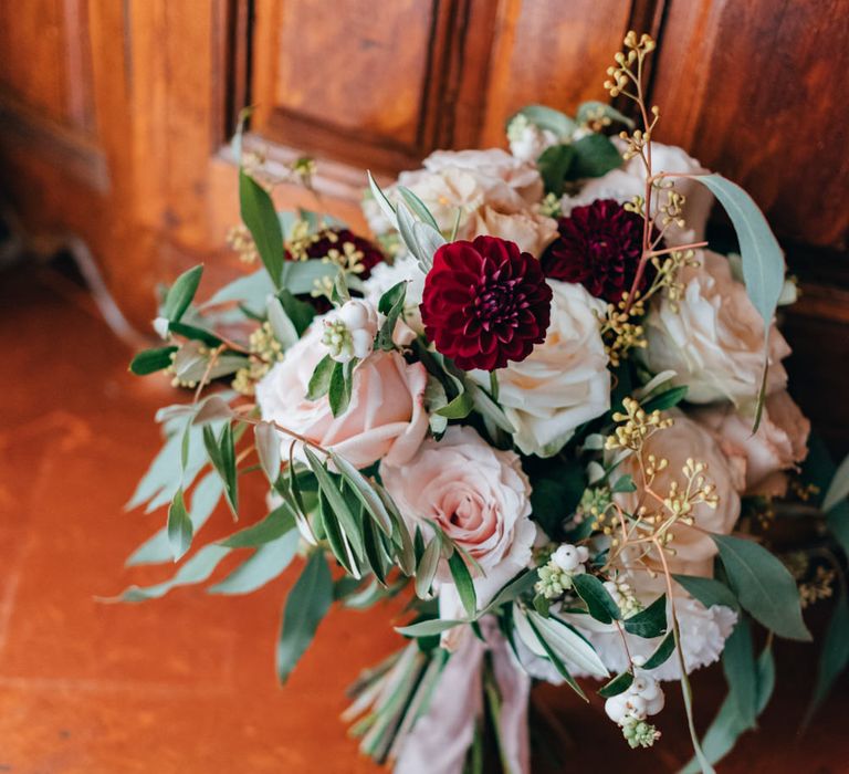 A bouquet of dark red dahlias, white and blush pink roses, olive leaves and wild foliage