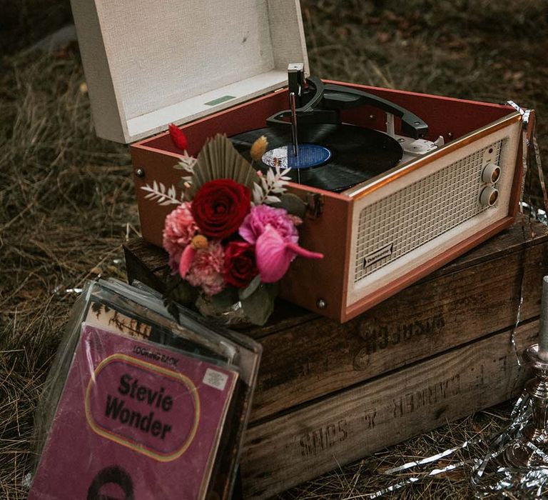 Record player box resting on wooden crate with records and tropical floral decor at festival themed wedding