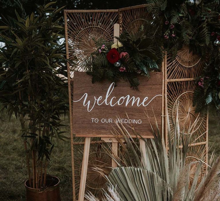 Wooden wedding welcome sign on easel in front of wooden screen with disco ball decor, pampas grass and palm leaves at festival themed wedding