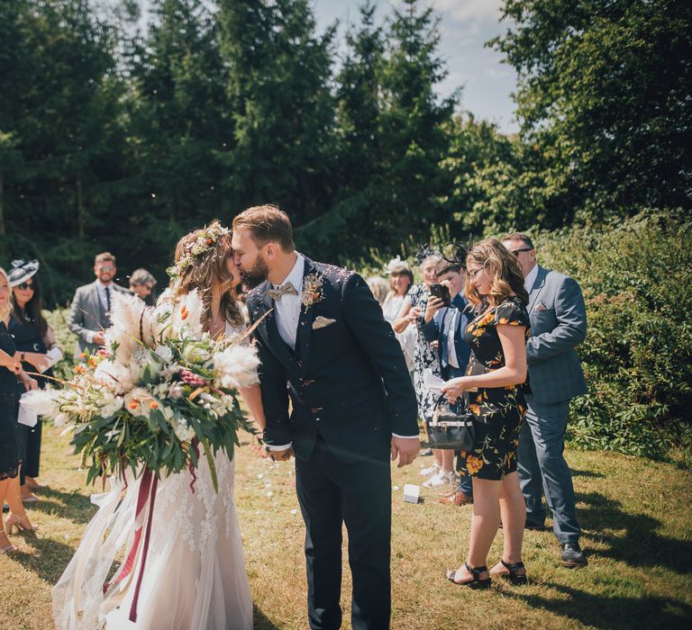 Bride & groom kiss outdoors at wedding ceremony in the sunshine