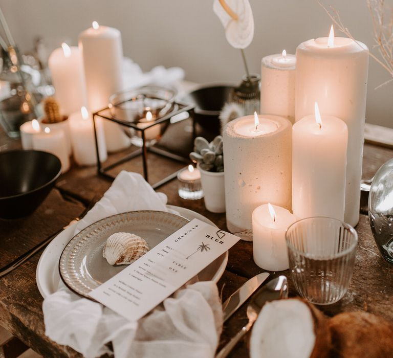 White pillar candles and tropical black and white neutral tablescape details including shells and coconut husks