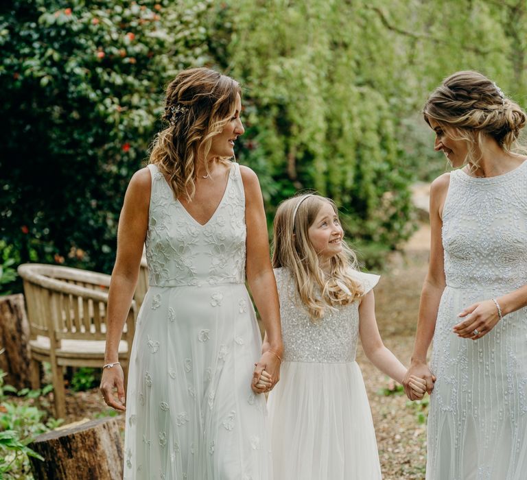 Brides hold hands with their daughter as they walk through gardens 