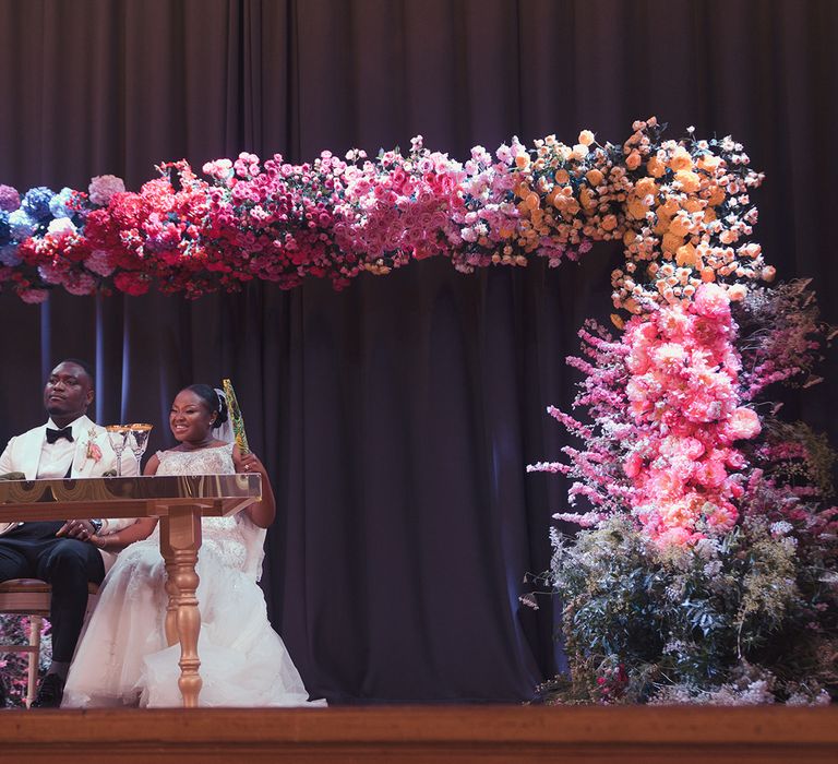 Bride & groom sit beneath floral arch on their wedding day