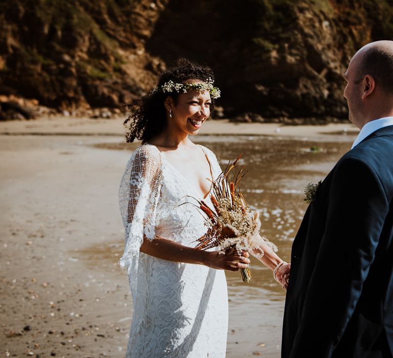 Bride & groom look lovingly at one another whilst bride smiles and holds her bouquet as the wind blows her hair