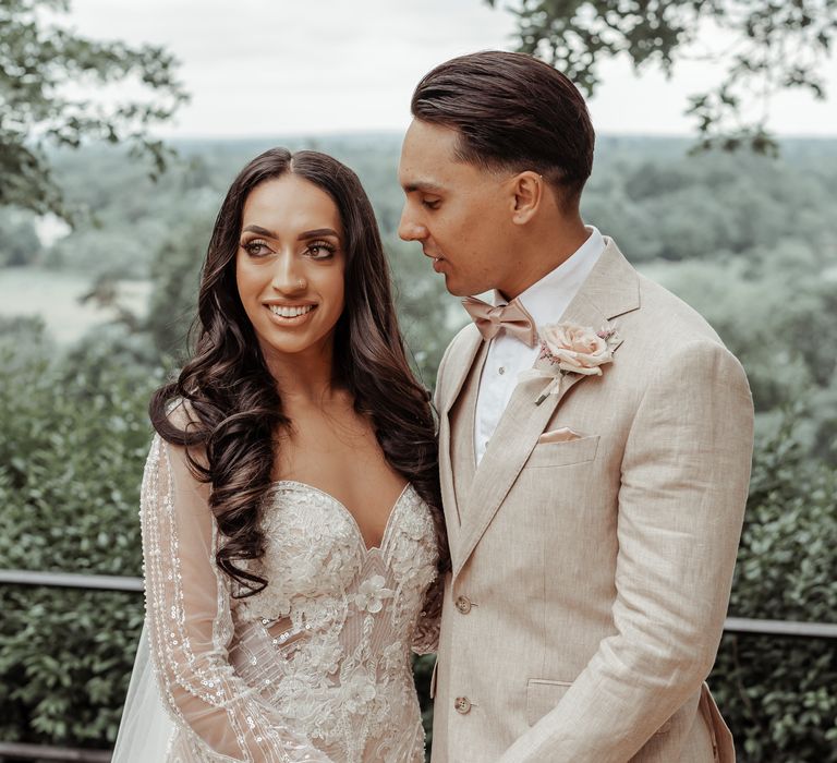 Groom looks lovingly at his bride who wears her dark hair in long and loose waves 