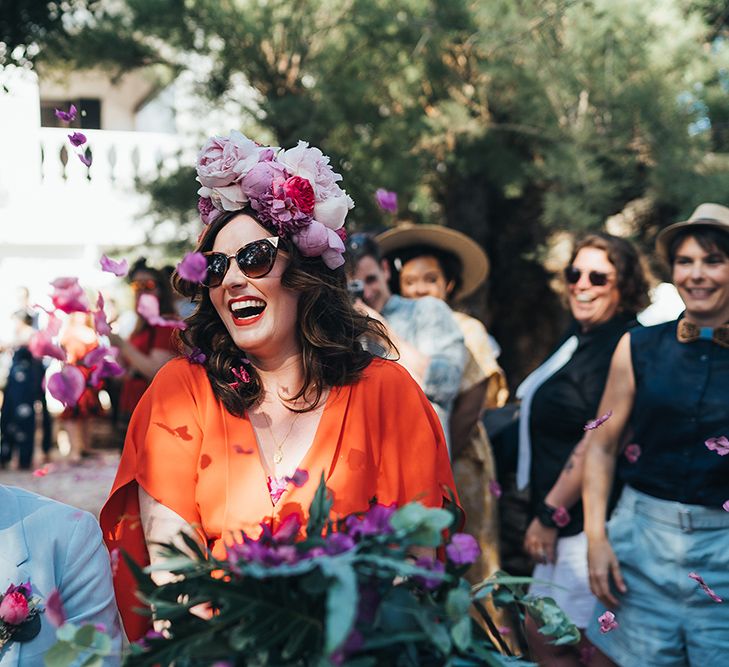 Bride walks through guests on her wedding day wearing her dark hair in curls and pink floral crown