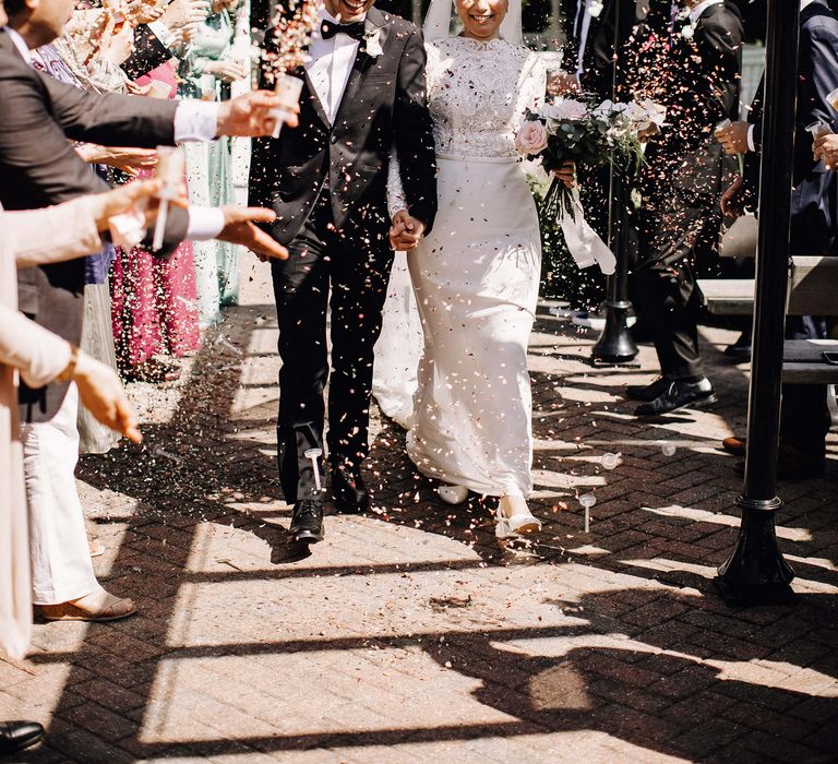 Bride and groom walking through confetti in white low heeled wedding shoes