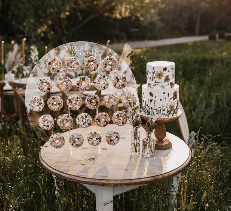 Flower pressed wedding cake on a wooden cake stand and doughnut wall on a round acrylic stand 