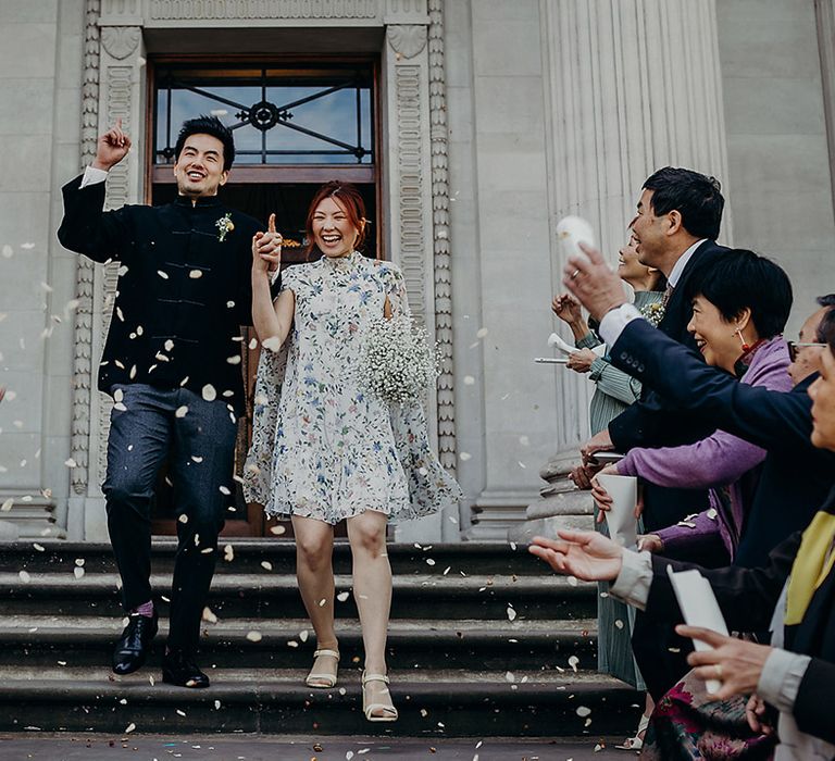 Confetti exit on the steps of Old Marylebone Town Hall with Bride in a short wedding dress with blue floral print holding a gypsophila wedding bouquet 